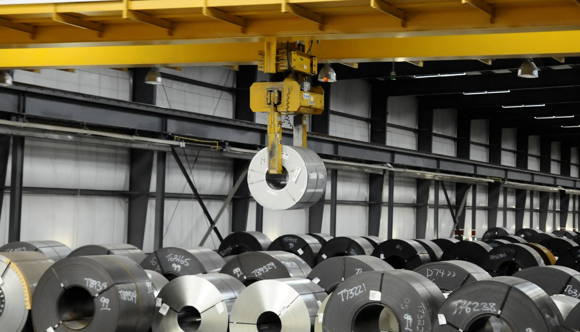 Overhead crane lifting a coil above a full coil storage bay